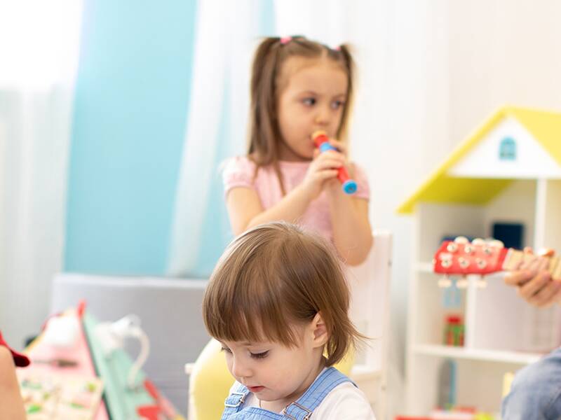 Kindergartenkinder sitzen und stehen, Musikinstrumente wie Flöte und Trommel spielend